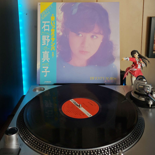 A vinyl record sits on a turntable. Behind the turntable, a vinyl album outer sleeve is displayed. The front cover shows Mako Ishino from the shoulders up looking off camera