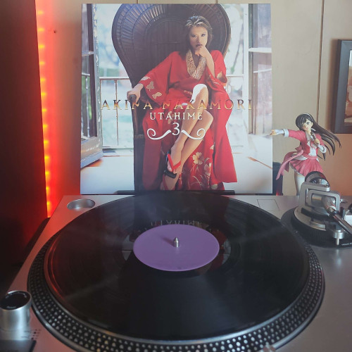 A vinyl record sits on a turntable. Behind the turntable, a vinyl album outer sleeve is displayed. The front cover shows in Akina Nakamori in a Kimono sitting in a large chair.