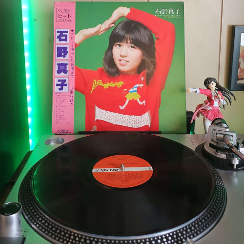 A vinyl record sits on a turntable. Behind the turntable, a vinyl album outer sleeve is displayed. The front cover shows Mako Ishino in a sweater holding her hands together above her head. 